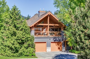 A modern two-story house with a large balcony, surrounded by dense evergreen trees. - Montebello 4864 - Private Hot Tub, Air Conditioning, Short Walk to the Village (Whistler)