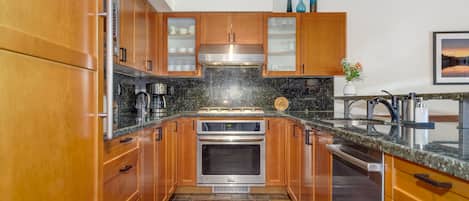A modern kitchen with wooden cabinets, stainless steel appliances, and a granite countertop.