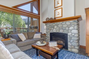 A cozy living room with a stone fireplace, a large window with a view of trees, and a comfortable seating area.