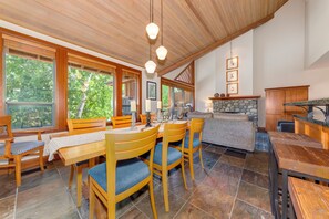 A spacious kitchen with wooden cabinets, a stone fireplace, and large windows offering a view of the outdoors. - Montebello 4864 - Private Hot Tub, Air Conditioning, Short Walk to the Village (Whistler)