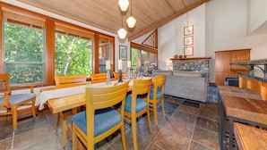A spacious kitchen with wooden cabinets, a stone fireplace, and large windows offering a view of the outdoors. - Montebello 4864 - Air Conditioning, Private Hot Tub, Mountain Views, Close to Village (Whistler)