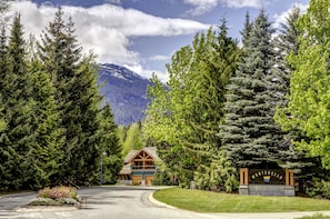A lodge with a mountain backdrop, surrounded by dense forest. - Montebello 4864 - Private Hot Tub, Air Conditioning, Short Walk to the Village (Whistler)