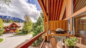 A wooden balcony with a view of a mountain, a barbecue grill, and a table with a bottle and a plant. - Montebello 4864 - Air Conditioning, Private Hot Tub, Mountain Views, Close to Village (Whistler)