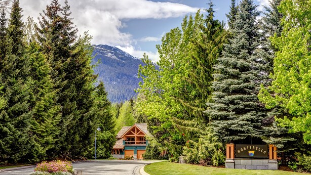 A lodge with a wooden exterior, surrounded by dense forest and mountains in the background. - Montebello 4864 - Air Conditioning, Private Hot Tub, Mountain Views, Close to Village (Whistler)