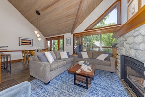 A modern living room with a sectional sofa, a fireplace, and a dining area with wooden chairs and a table. - Montebello 4864 - Private Hot Tub, Air Conditioning, Short Walk to the Village (Whistler)