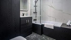 Un baño moderno con tocador de madera oscura, ducha envuelta en vidrio y suelo de mármol.