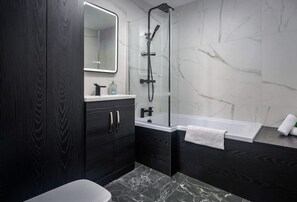 Un baño moderno con tocador de madera oscura, ducha envuelta en vidrio y suelo de mármol.