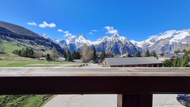 A mountain landscape with snow-capped peaks, a clear sky, and a parking area with a building in the foreground. - Bright studio for 4 people with magnificent view (Les Deux Alpes)