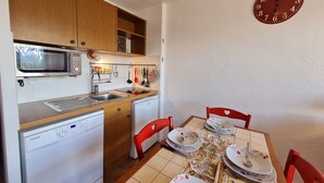 A compact kitchen with a microwave, sink, and dishwasher, a dining table set with plates and cutlery, and a wall clock. - Bright studio for 4 people with magnificent view (Les Deux Alpes)
