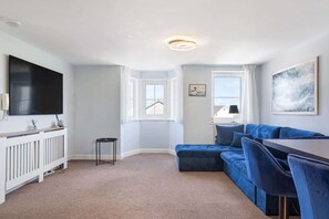 A modern living room with a sectional sofa, a flat-screen TV, a dining area, and a large window. - Cosy Apartment, Parking, Central Newquay (Newquay)