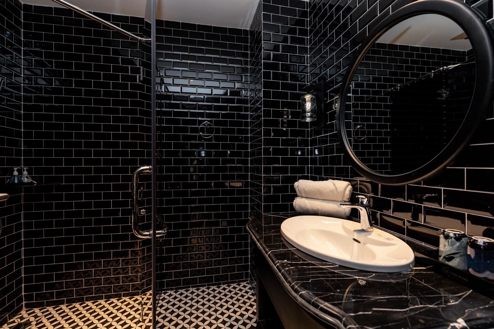A bathroom with black tiled walls, a white sink, and a round mirror.