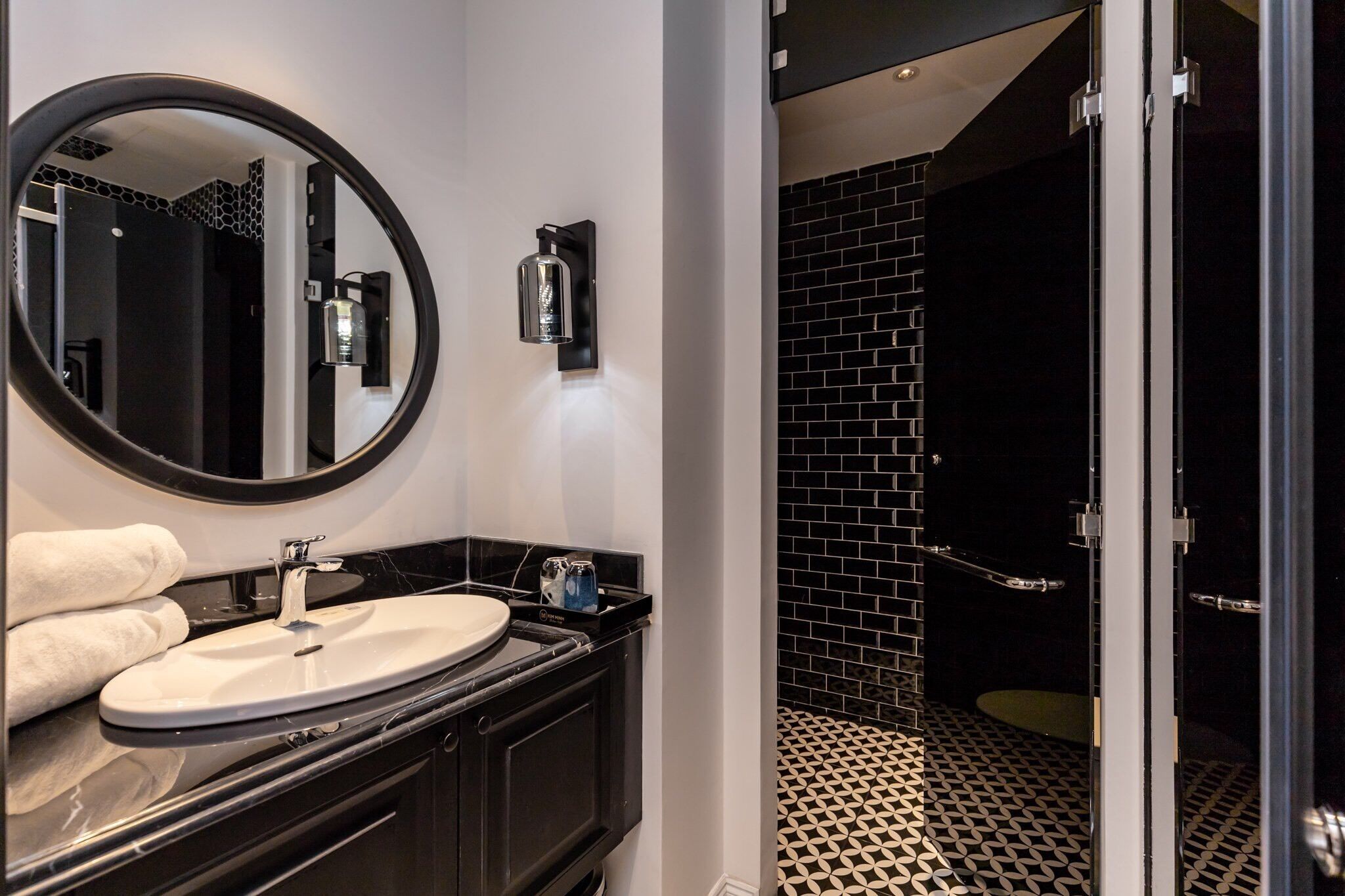 A modern bathroom with a round mirror, a sink, and a black-tiled shower area.