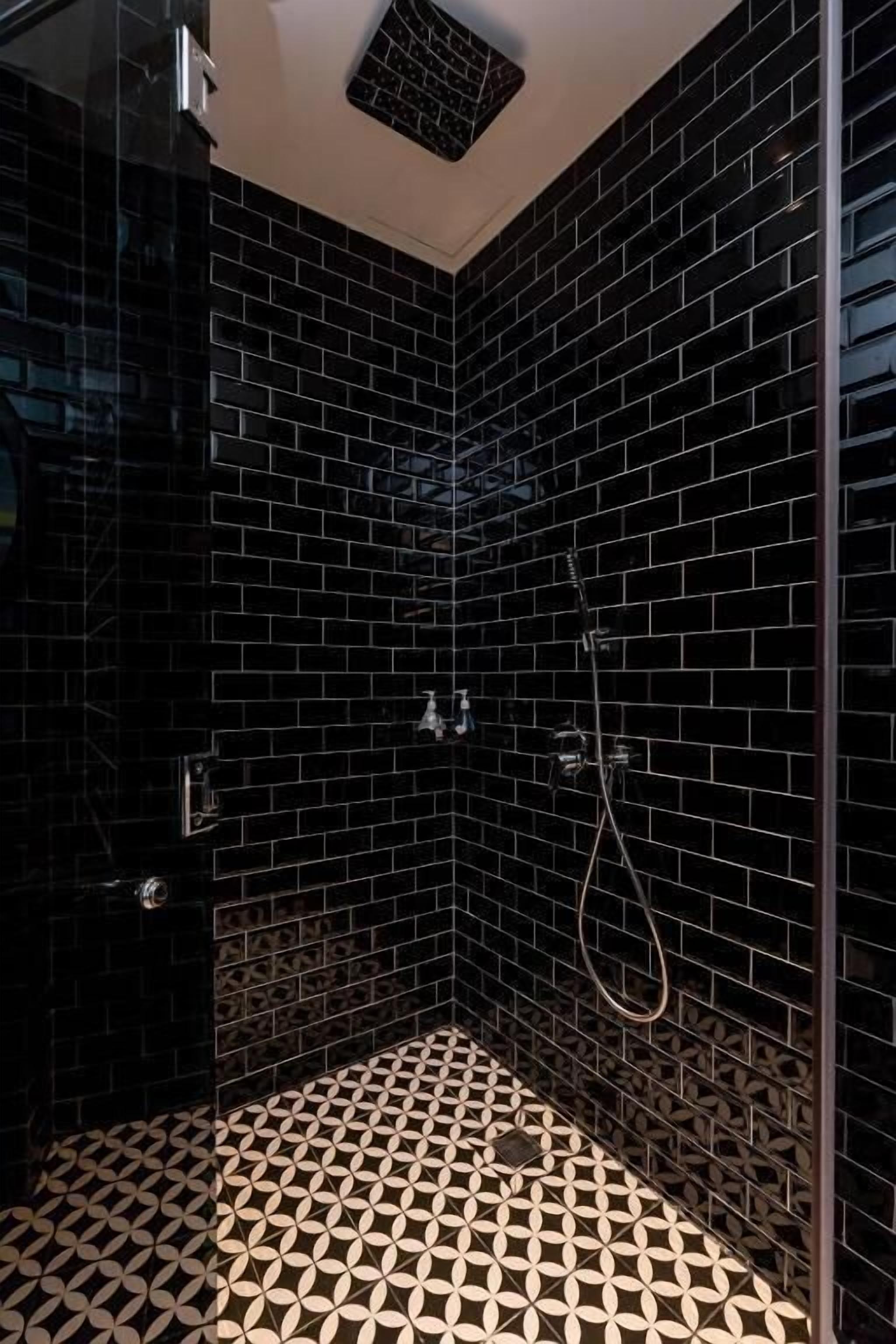 A shower with black tiles and a geometric patterned floor.
