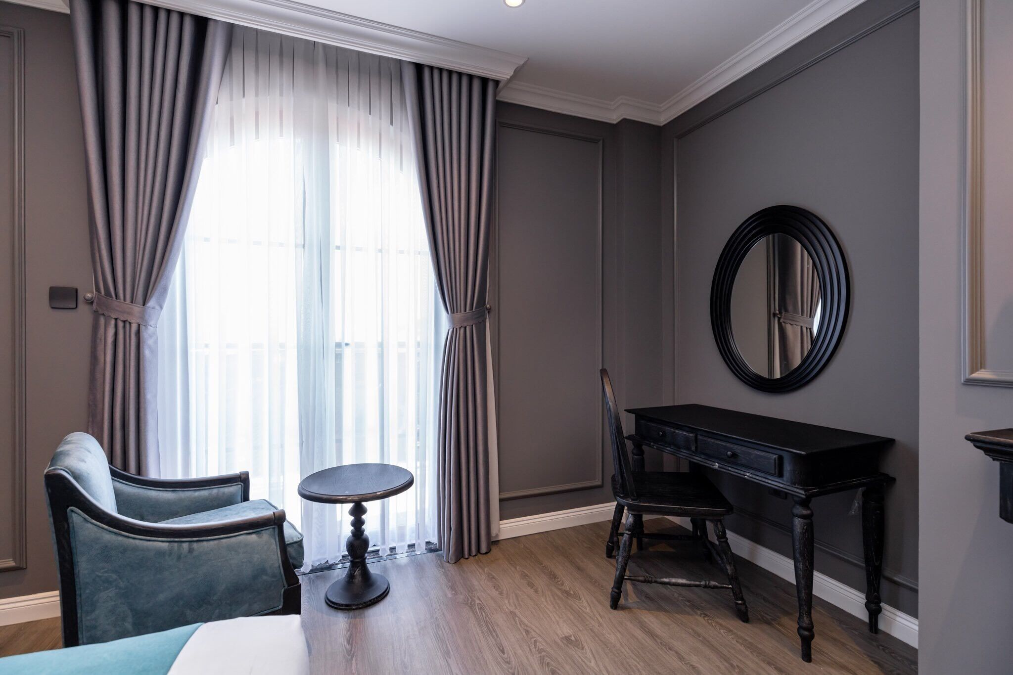 Une pièce comprenant un lit, deux chaises, une petite table ronde, un bureau et un miroir au mur.