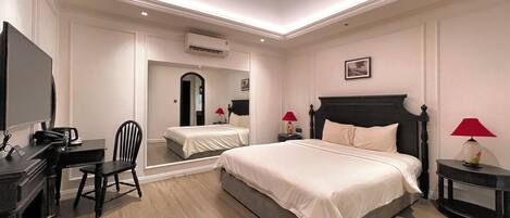A hotel room with a bed, a desk with a chair, a TV, a mirror, and a ceiling light.