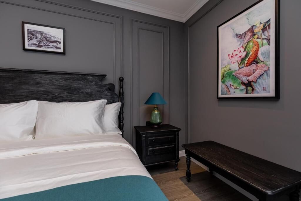 A bedroom with a bed, a nightstand, a bench, and two framed artworks on the wall.