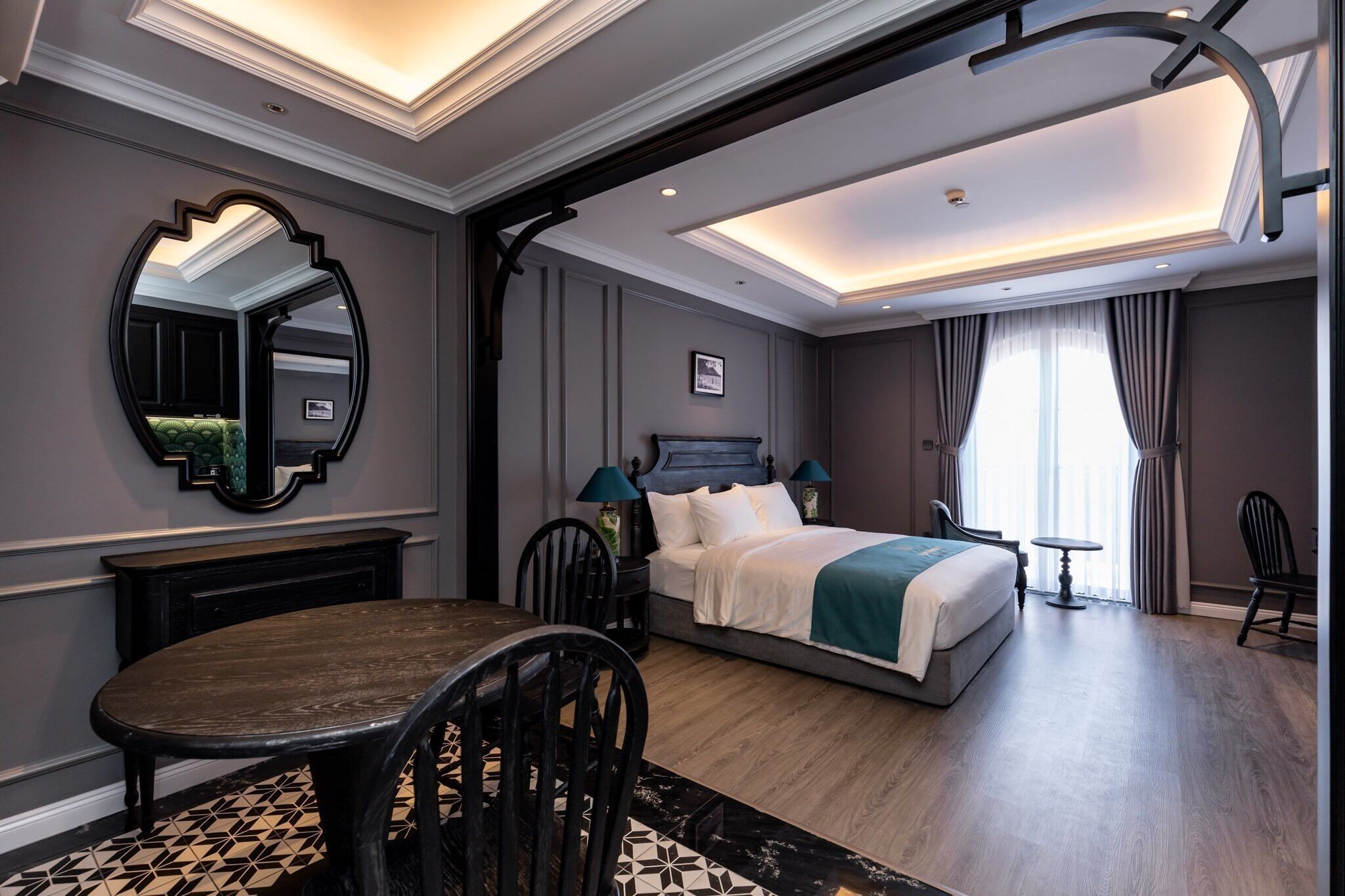A hotel room with a large bed, a dining table, a mirror, and a view of the outside.
