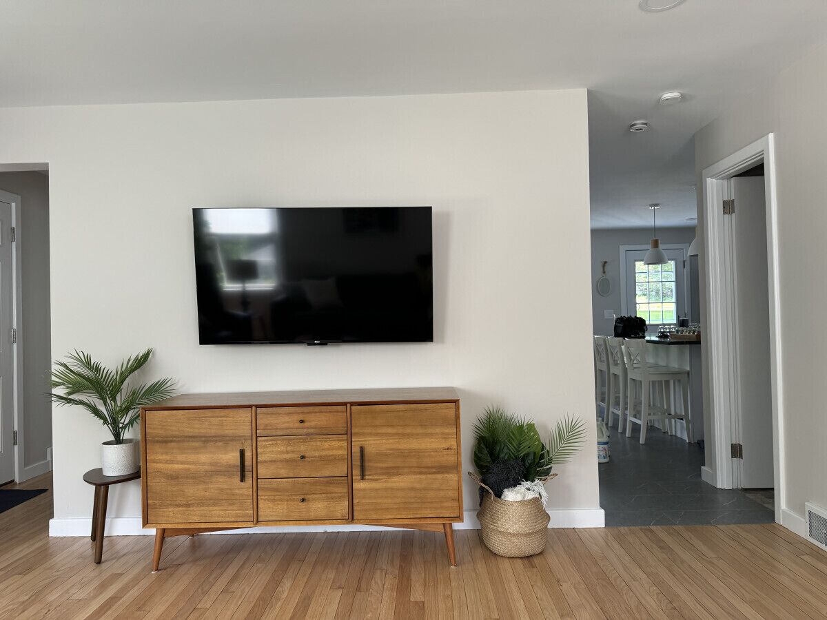 A modern living room with a wooden cabinet, a flat-screen TV mounted on the wall, and a potted plant on the floor.