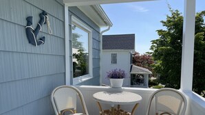 A covered porch with two wicker chairs and a small table, a potted plant, and a decorative rope sculpture. - The Blue Anchor House · walk Mystic-Train/Aquarium (Stonington)