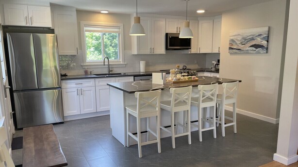 A modern kitchen with white cabinets, stainless steel appliances, and a central island with bar stools. - The Blue Anchor House · walk Mystic-Train/Aquarium (Stonington)