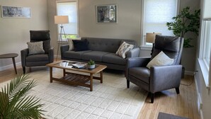 A living room with a grey sofa, two armchairs, a coffee table, and a floor lamp. - The Blue Anchor House · walk Mystic-Train/Aquarium (Stonington)