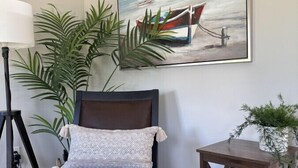 A bedroom with a bed, a bedside table, a floor lamp, a potted plant, and a painting of a boat on water. - The Oar Cottage (24) · walk Mystic-Train/EV Lvl-2 (Stonington)