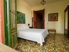 A room with a bed, a bench, a painting, and a door.