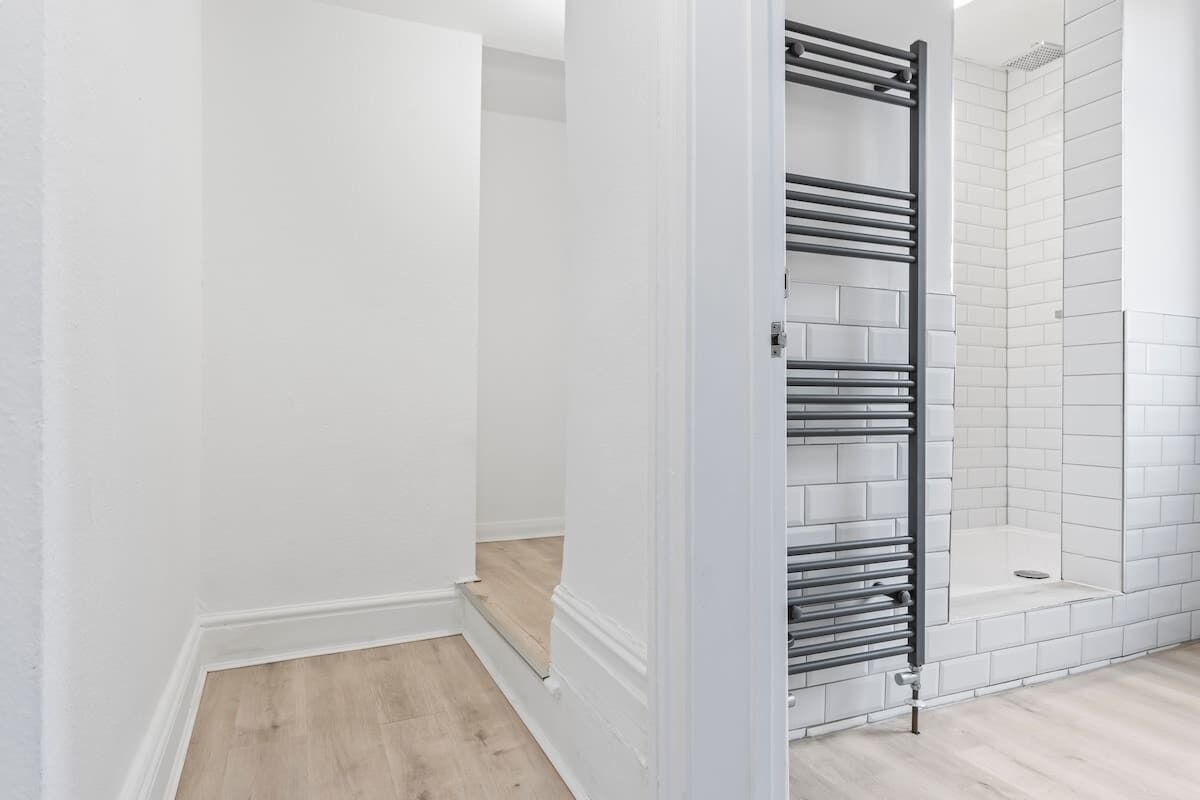 Een badkamer met witte wanden, een betegeld douchegedeelte en een metalen handdoekhouder.