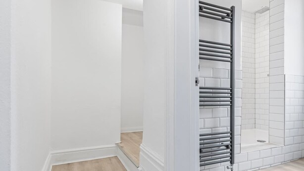 Une salle de bain aux murs blancs, avec une douche carrelée et un porte-serviettes en métal.