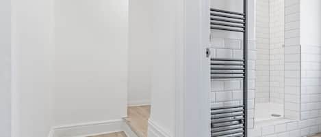 A bathroom with white walls, a tiled shower area, and a metal towel rack.