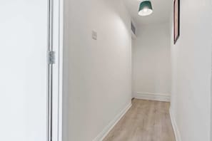 Un couloir étroit aux murs blancs et au plancher en bois.