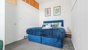 Une chambre à coucher avec un lit bleu, des murs blancs et deux tableaux encadrés.