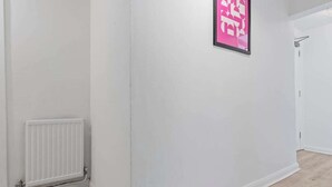 A hallway with a radiator, a framed poster on the wall, and a door at the end. - Cedar View – 2 Bed Apartment (Newport)