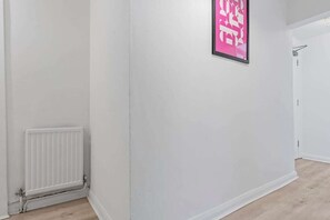 A hallway with a radiator, a framed poster on the wall, and a door at the end.