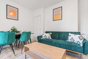 Una sala de estar moderna con un sofá verde, una mesa de centro de madera y un comedor con sillas verdes.