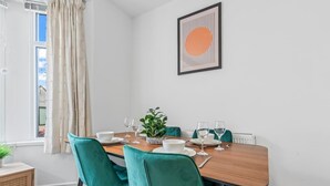 Un coin repas avec une table en bois, des chaises de couleur turquoise, des assiettes blanches et une plante en pot.