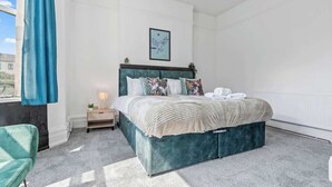 Une chambre à coucher avec un lit, une table de chevet, une chaise bleue et une fenêtre avec un rideau.