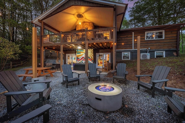 A wooden cabin with a covered deck, outdoor seating, and a fire pit.