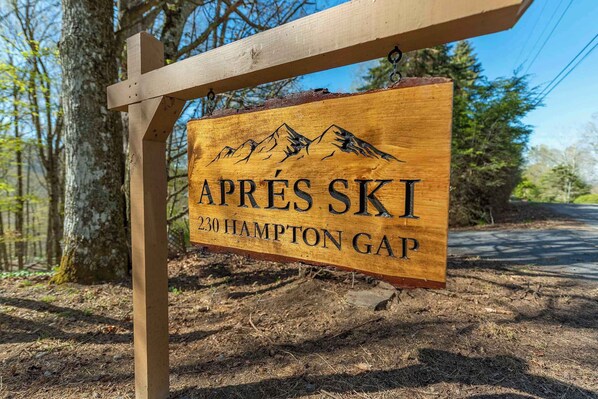 A wooden sign with 'APRES SKI' and '230 HAMPTON GAP' engraved on it, mounted on a wooden post.