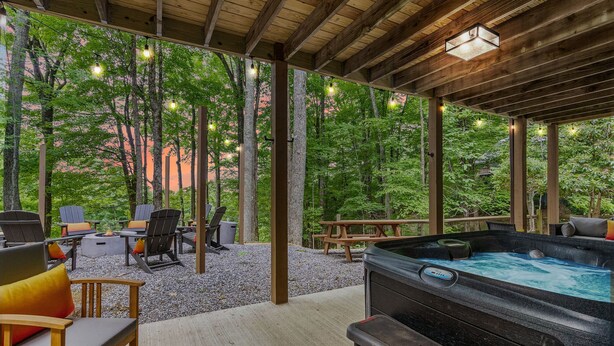 Un espace extérieur aménagé avec des chaises et un jacuzzi, le tout installé sous une pergola en bois illuminée de guirlandes lumineuses.