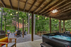 An outdoor seating area with chairs and a hot tub under a wooden pergola with string lights.