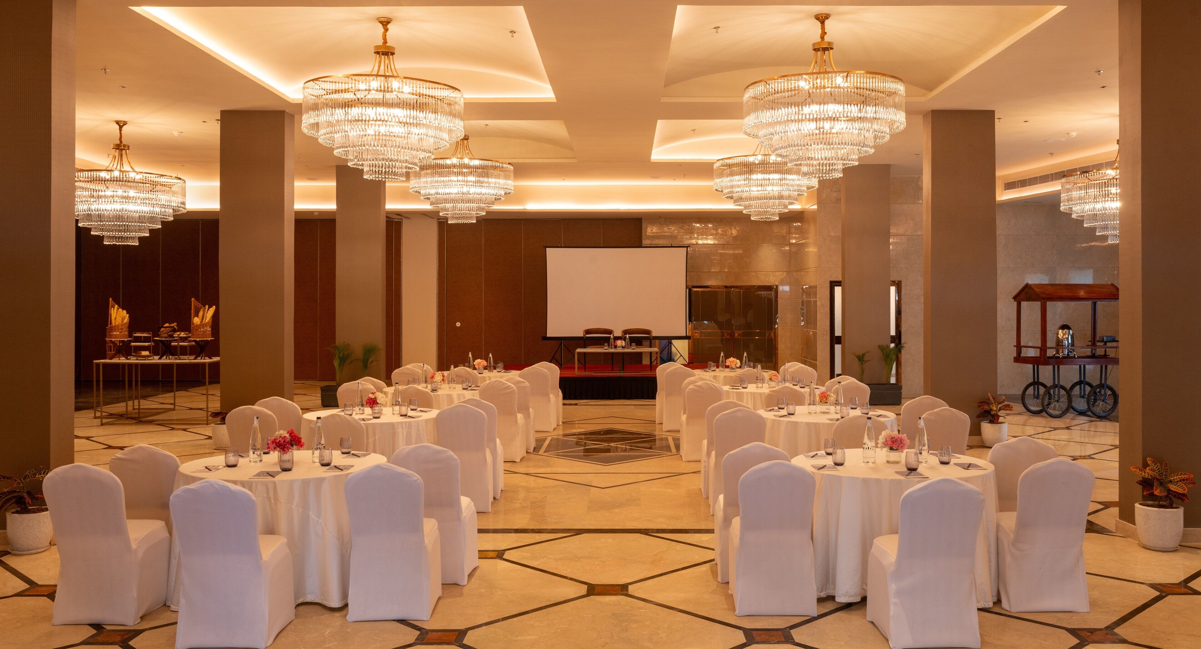 A banquet hall with round tables, white chairs, and chandeliers.