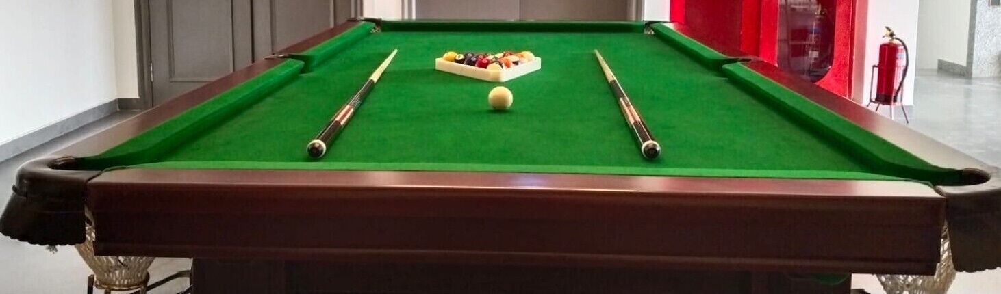A pool table with a green felt surface, two cue sticks, and a set of billiard balls.