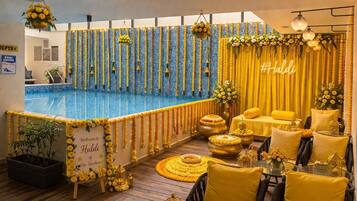 A pool area with a blue-tiled floor, yellow and white floral decorations, and a sign welcoming guests to Haldi.