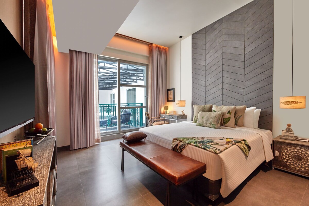 A hotel room with a large bed, a bench, a TV, a balcony with a view, and a modern wall design.