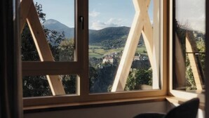 Ein Zimmer mit großem Fenster und Blick auf eine gebirgige Landschaft sowie ein Dorf darunter.
