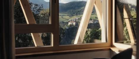 A room with a large window offering a view of a mountainous landscape and a village below.