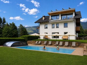 Una casa moderna de dos pisos con piscina, mobiliario exterior y vistas a las montañas.