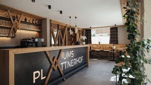 Ein modernes Interieur mit einer Rezeption mit dem Schild "PLIMS TNNERHOF", Holzböden, Pendelleuchten und einer Sitzecke.