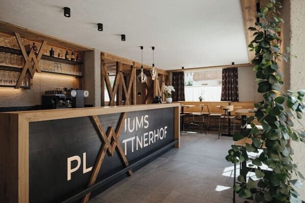 A modern interior with a reception desk labeled "PLIMS TNNERHOF," wooden shelves, hanging lights, and a seating area.